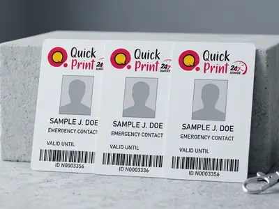 Three white PVC identity cards with photo and barcode propped upright beside a navy lanyard, printed in Hyderabad