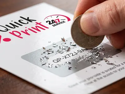 Hand scratching the silver panel of a promotional scratch card to reveal a unique code, printed in Hyderabad by QuickPrintt